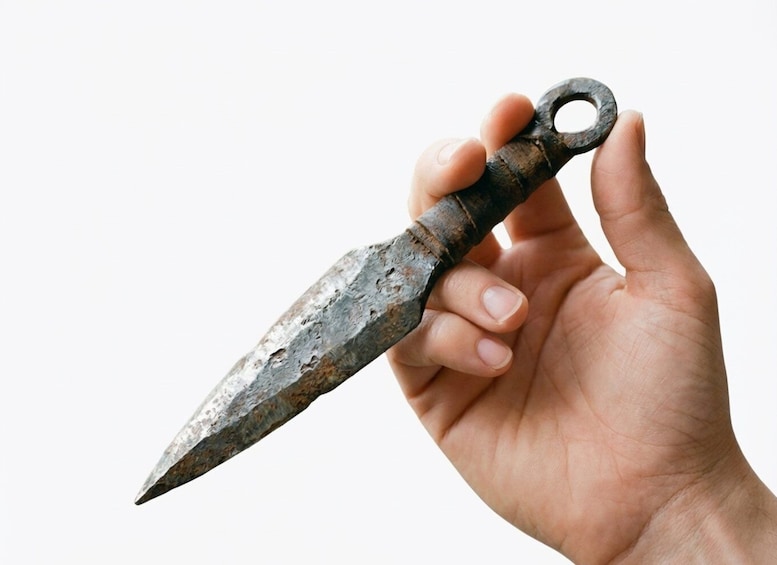 A hand holding an ancient, rusted metal knife with a ring handle. 2