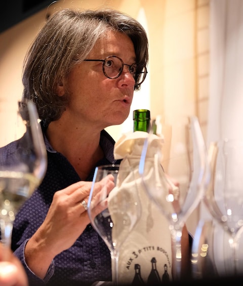 A person holding a wine bottle with a label that reads 'Aux 3 O TITS.' 1
