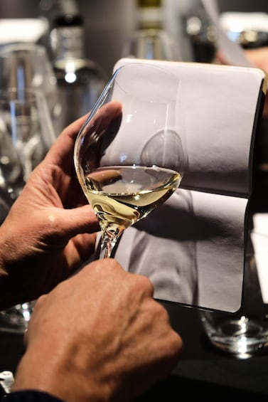 A person holding a wine glass with a white liquid, likely wine, and a menu or list in front of them. 2