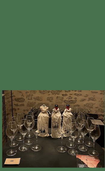 A table with wine glasses and three bottles of wine in cloth bags. 4