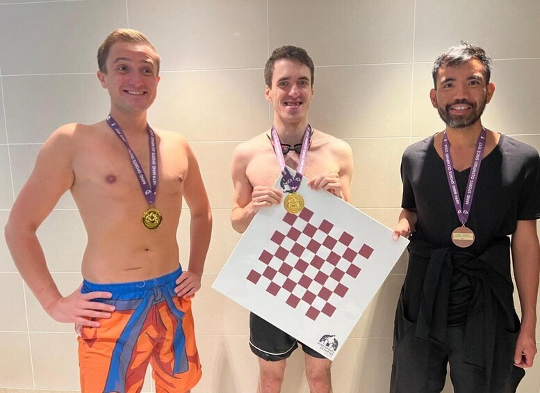 Three individuals holding a chessboard, each wearing a medal. 1