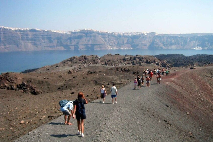 A group of people walking on a rocky path with a body of water and cliffs in the background. 3