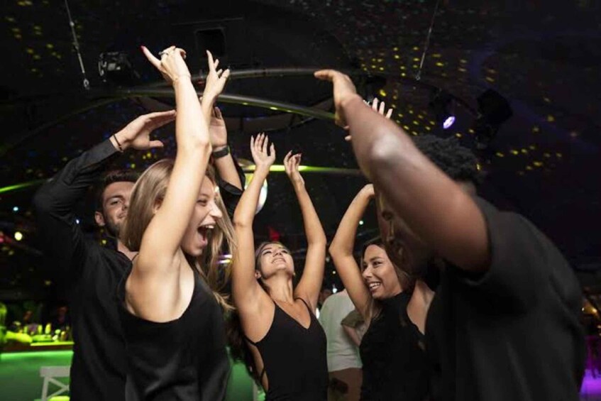 A group of people dancing at a nightclub with a DJ booth and stage lighting. 3