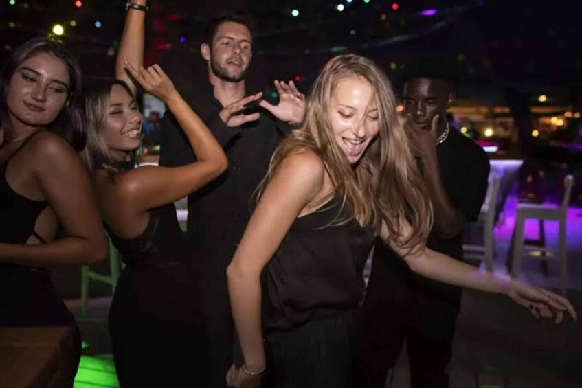 A group of people dancing at a party with colorful lights in the background. 1
