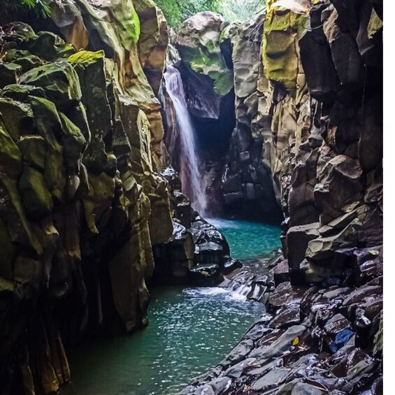 A waterfall cascading into a clear pool surrounded by rocky terrain. 1