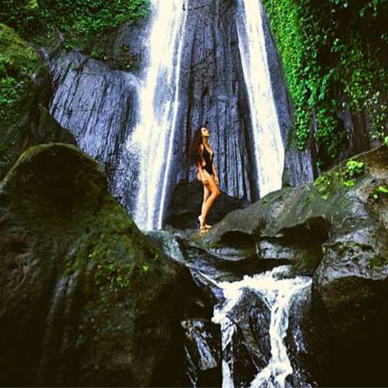 A waterfall with a person standing on a rock in the foreground. 3