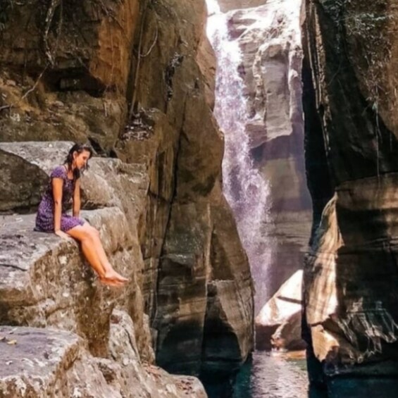A person sitting on a rock by a waterfall. 4