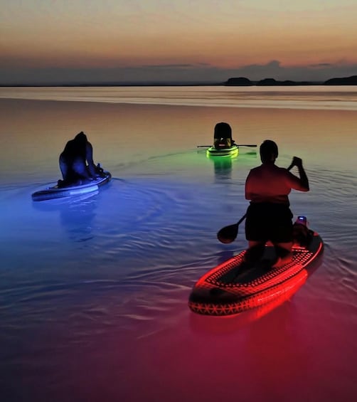 Three kayaks on a calm body of water at dusk with colorful lights. 1