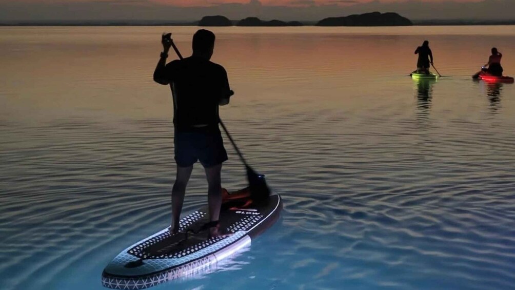 A person paddleboarding on calm water during twilight with distant landforms. 2