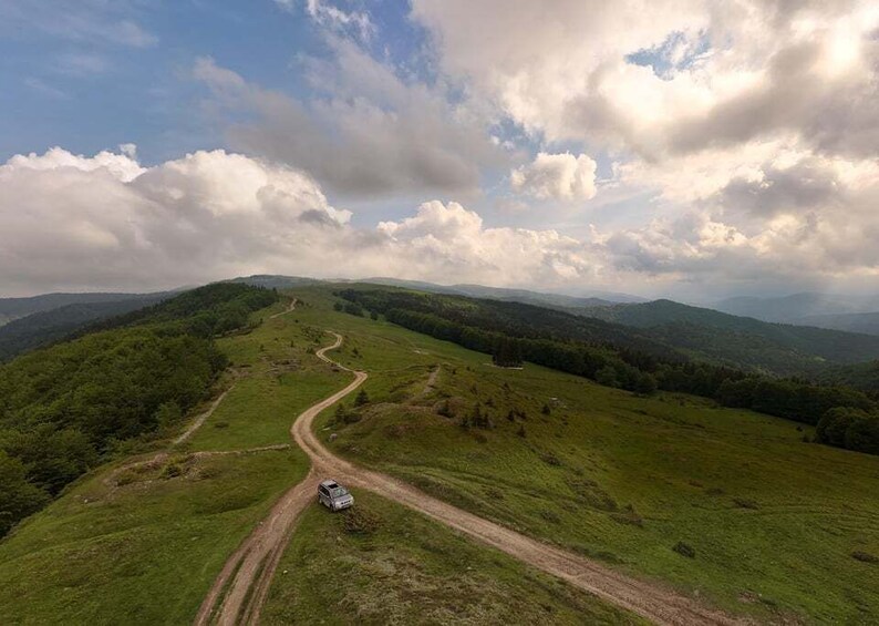 A winding road through a hilly landscape with a vehicle parked on the side. 3
