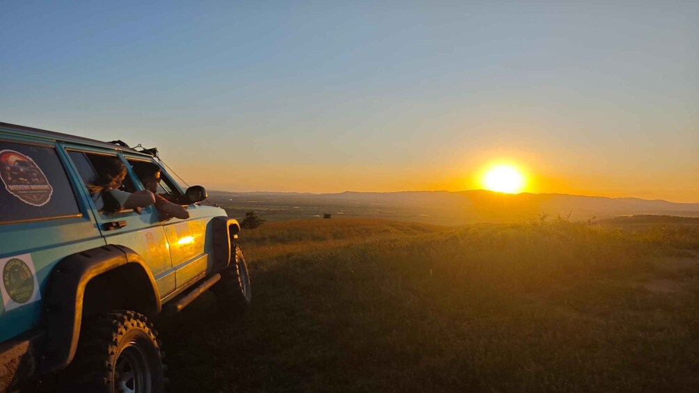 A vehicle on a grassy hill with a sunset in the background. 1