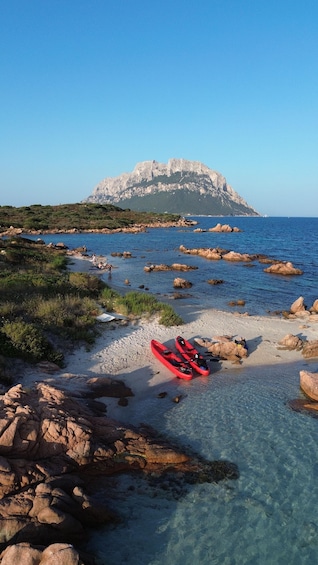 A rocky shoreline with kayaks and a mountain in the background. 2