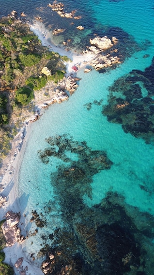 An aerial view of a coastal area with clear turquoise waters, rocky outcrops, and a sandy beach. 5