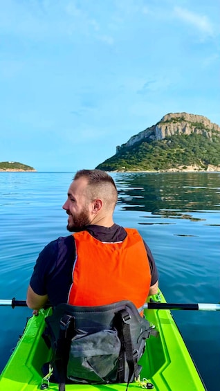 A person in a kayak on calm water with a mountainous island in the background. 1