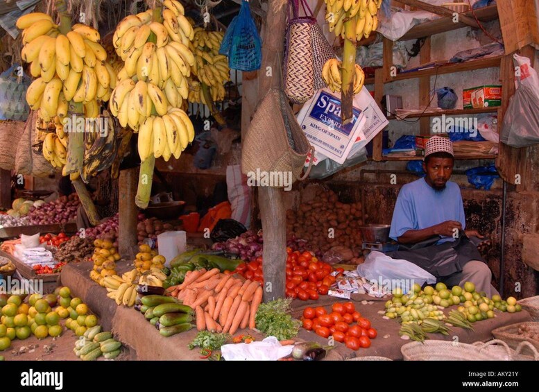 A market stall with bananas, vegetables, and a man sitting. 4