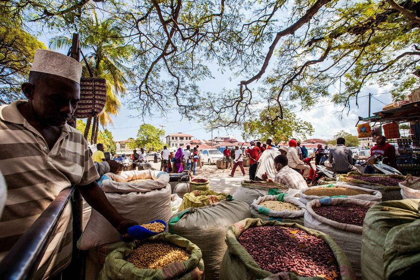 A bustling outdoor market with people buying and selling goods, surrounded by trees and buildings. 5