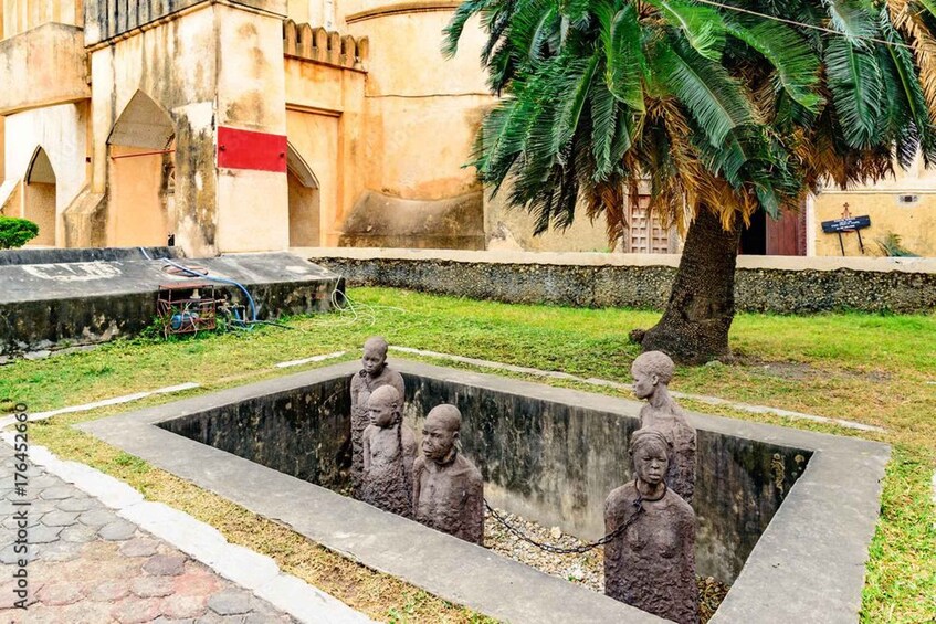 A statue of a child in a concrete basin surrounded by grass and a palm tree. 2