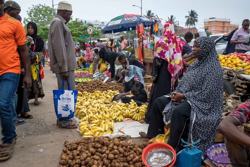 A bustling outdoor market with people selling and buying goods, including bananas and potatoes. 3
