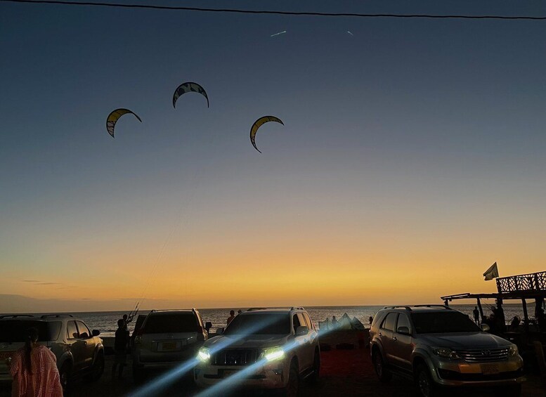 A sunset with kites flying, parked cars, and a beach. 4