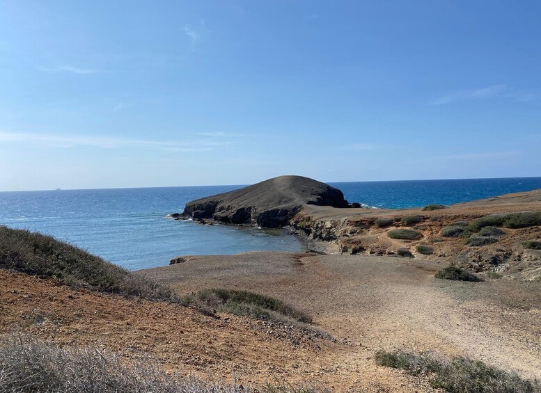 A coastal landscape with a prominent hill, a clear sky, and the ocean. 3