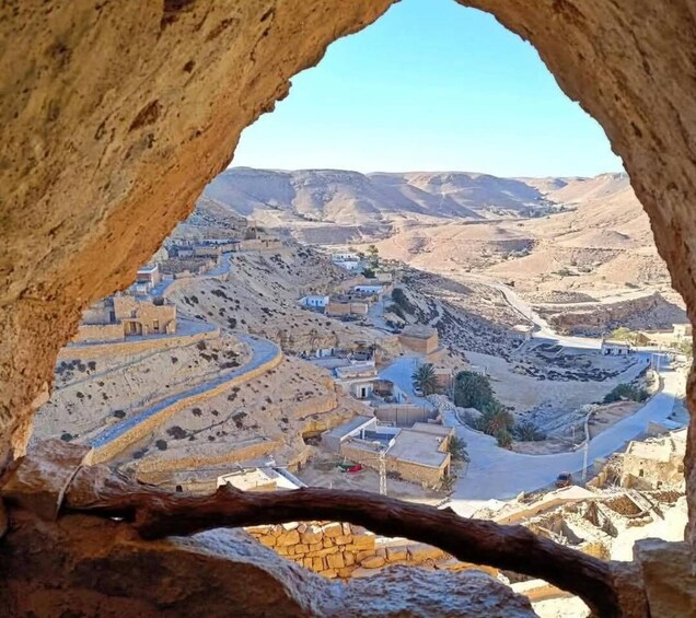 A view through a cave opening of a desert landscape with scattered buildings and winding roads. 2