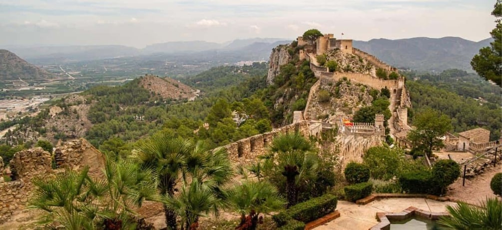 A historic fortification on a hill with surrounding greenery and distant landscapes. 1