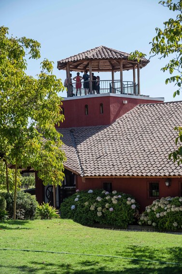 A red building with a tiled roof, a covered wooden structure on top, and lush green landscaping. 3