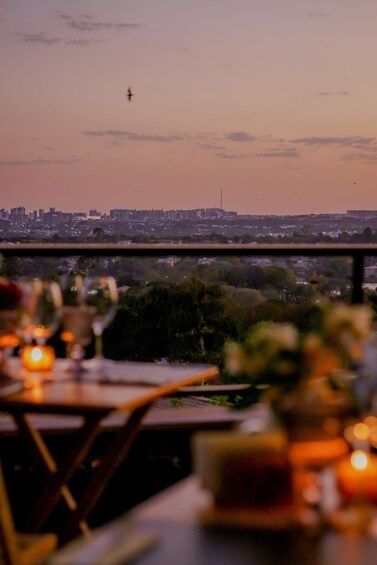 A city skyline at dusk with a bird flying in the sky, viewed from a dining area with tables and candles. 2