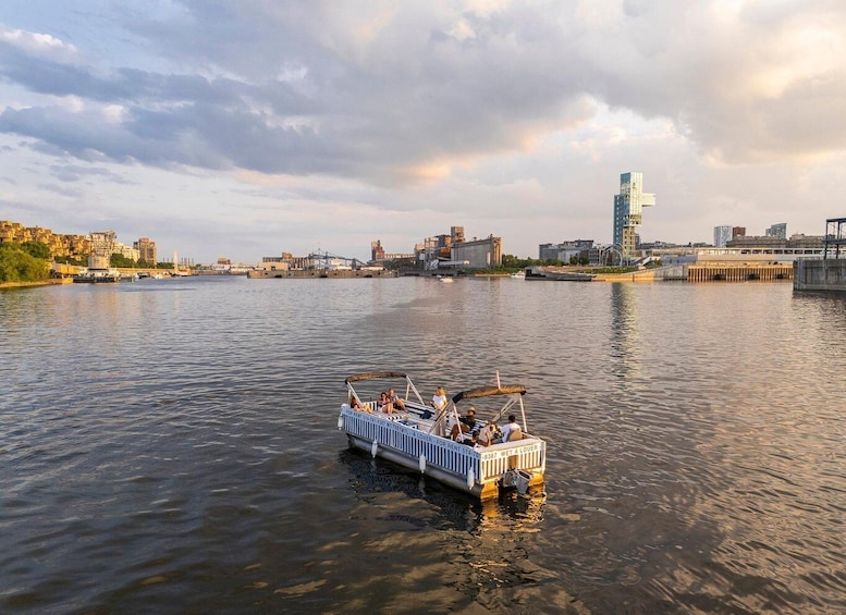 A boat with people on a river, a city skyline in the background, and a cloudy sky. 1