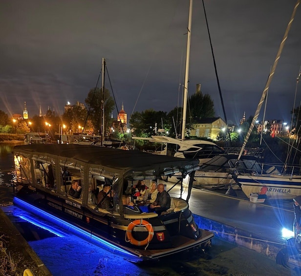 A river cruise boat with passengers, docked at a marina with other boats and a cityscape in the background. 3