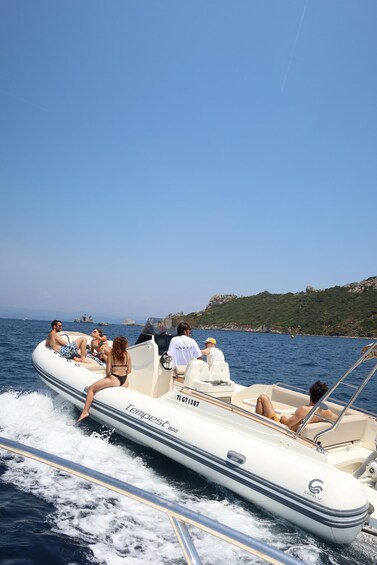A group of people on a white inflatable boat with 'Tempest 900' written on it, cruising on a body of water with a rocky coastline in the background. 2