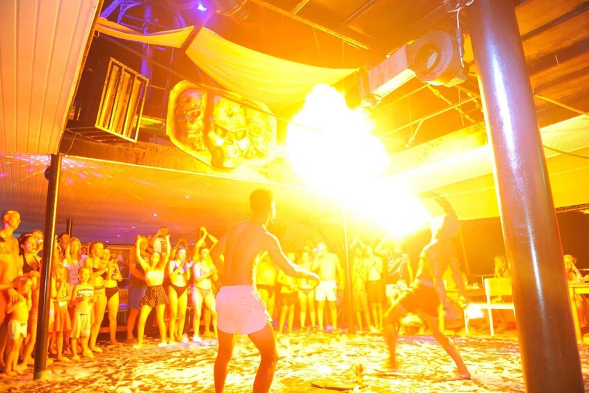 A group of people dancing on a beach with a large fire in the background. 5