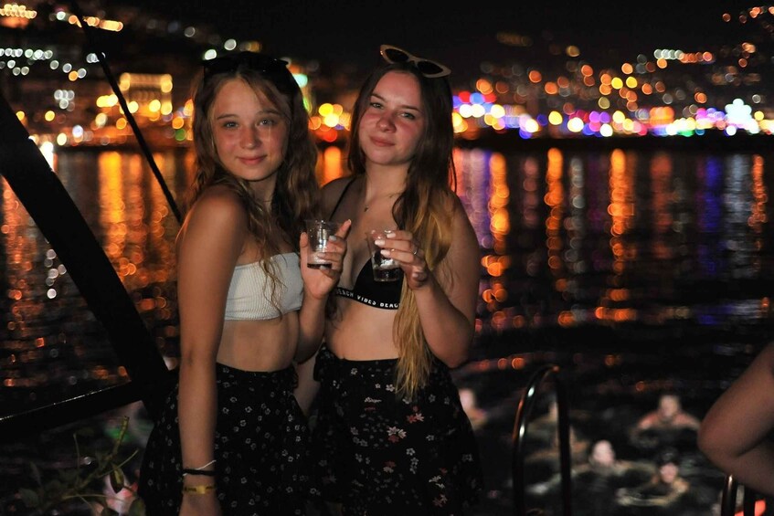 Two people standing by a waterfront with city lights in the background. 3