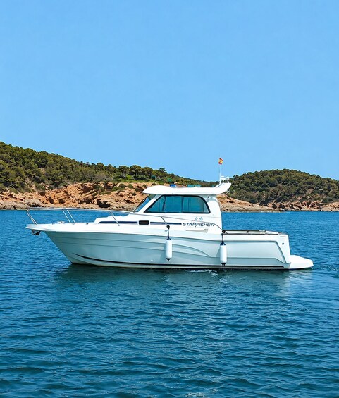 A white boat named 'STARFISHER' on calm blue water with a rocky shoreline and green trees in the background. 5