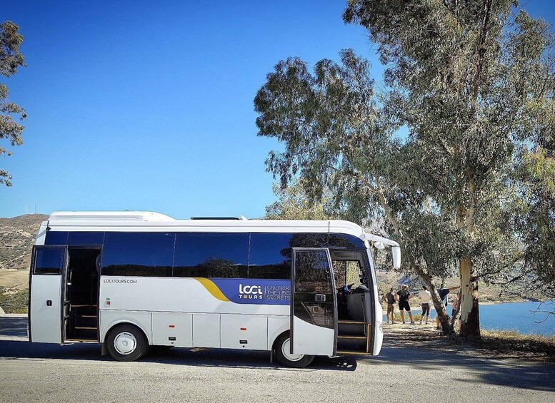 En hvid turistbus parkeret ved en sø med træer og mennesker i baggrunden. 5