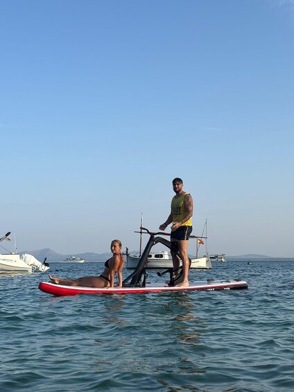Two people on a paddleboard in a calm body of water with boats and mountains in the background. 4