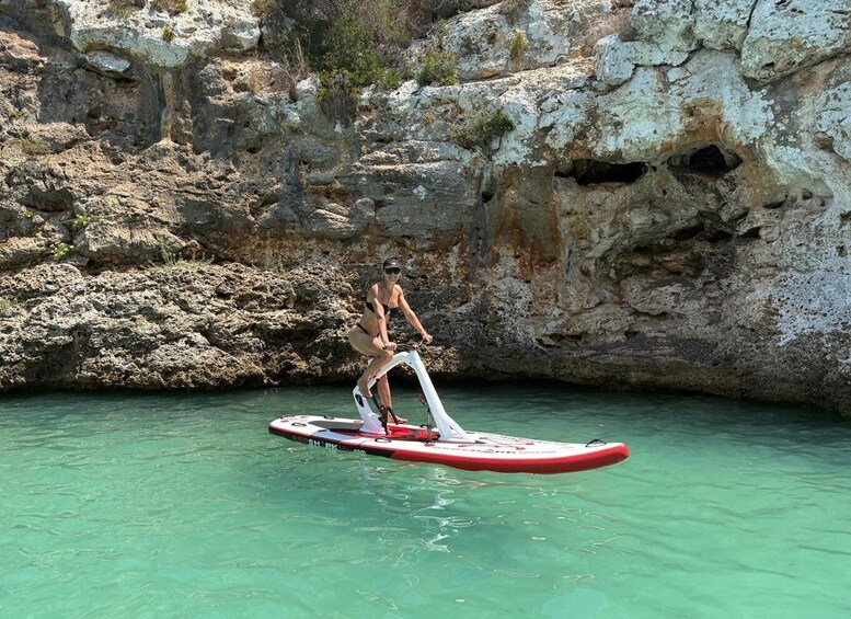 A person riding a red and white paddleboard in clear water near rocky cliffs. 2