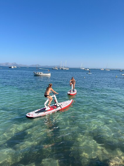 Two people paddleboarding on a clear blue sea with boats in the background. 3