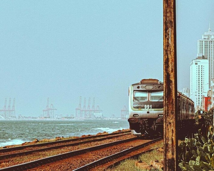 A train on tracks near a body of water with industrial structures in the background. 5