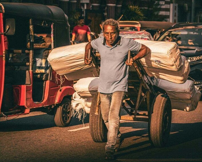 A man pushing a cart with large sacks, a red auto-rickshaw, and a car in the background. 4
