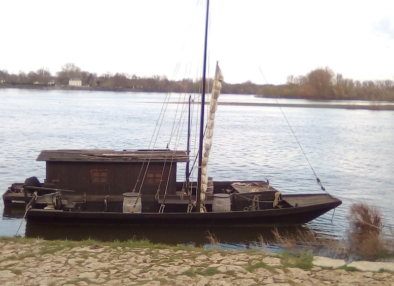 A small boat docked at a rocky shore with a building on board and a calm river in the background. 4