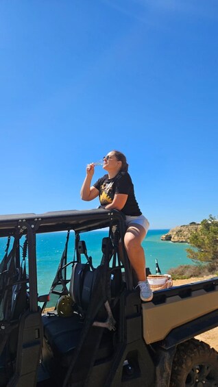 A person sitting on a vehicle with a clear view of the ocean and rocky terrain. 4