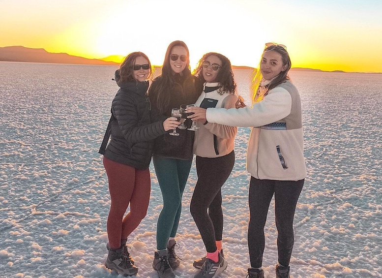 Four people toasting with drinks in a snowy landscape at sunset. 1