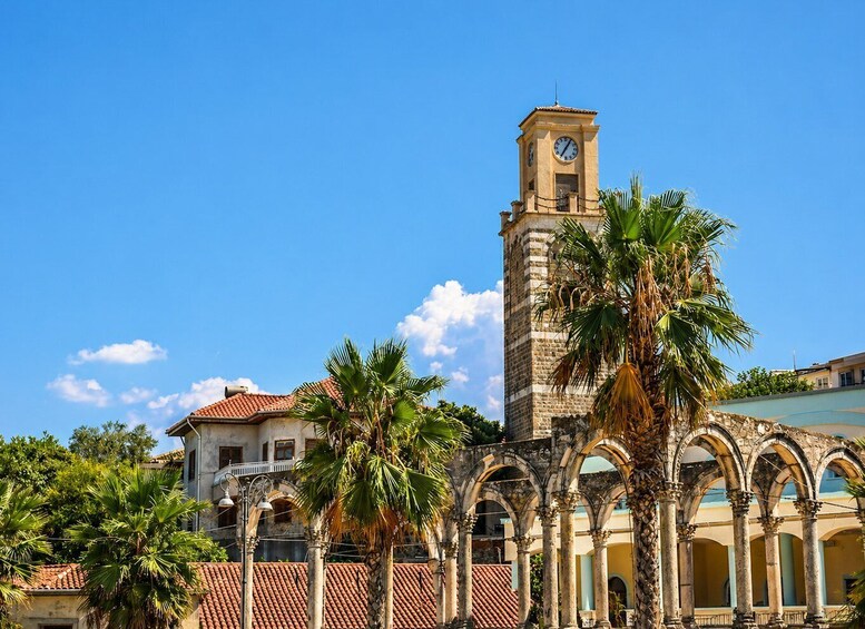 A historic building with a clock tower, palm trees, and an arched courtyard. 1