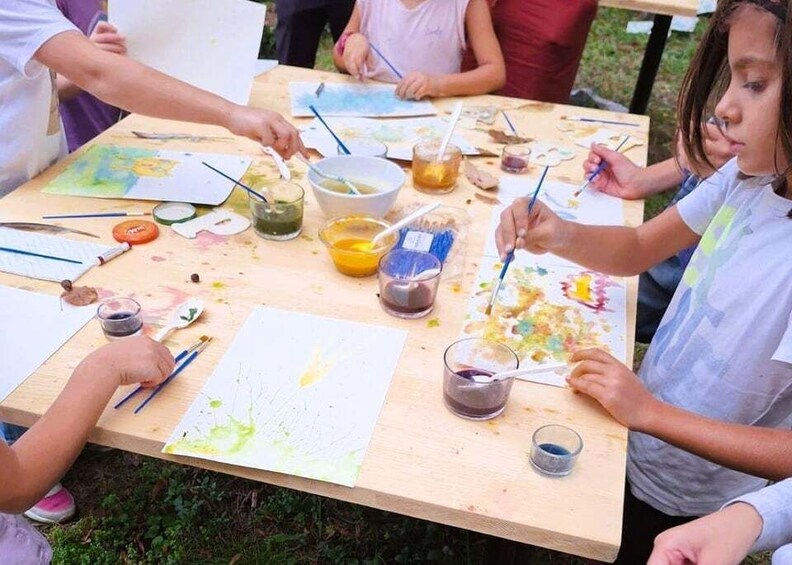 Children painting on easels at an outdoor table with art supplies. 1