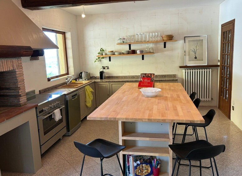 A kitchen with a wooden table, black chairs, a brick oven, and shelves with glassware. 5