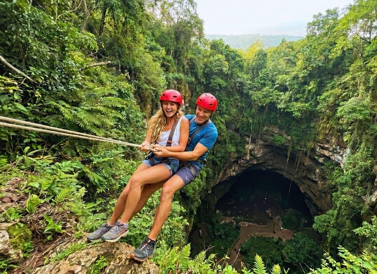 Dos personas descendiendo en rápel a una cueva exuberante y verde. 1