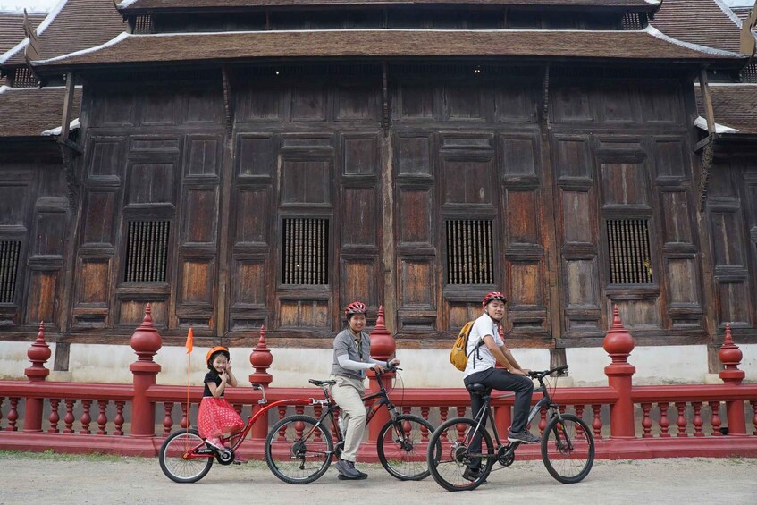 A wooden building with a red railing and people riding bicycles. 1
