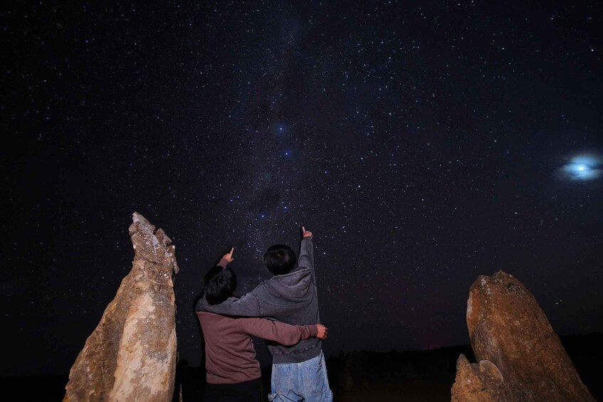 Two people pointing at stars in the night sky, with large rocks on either side. 2