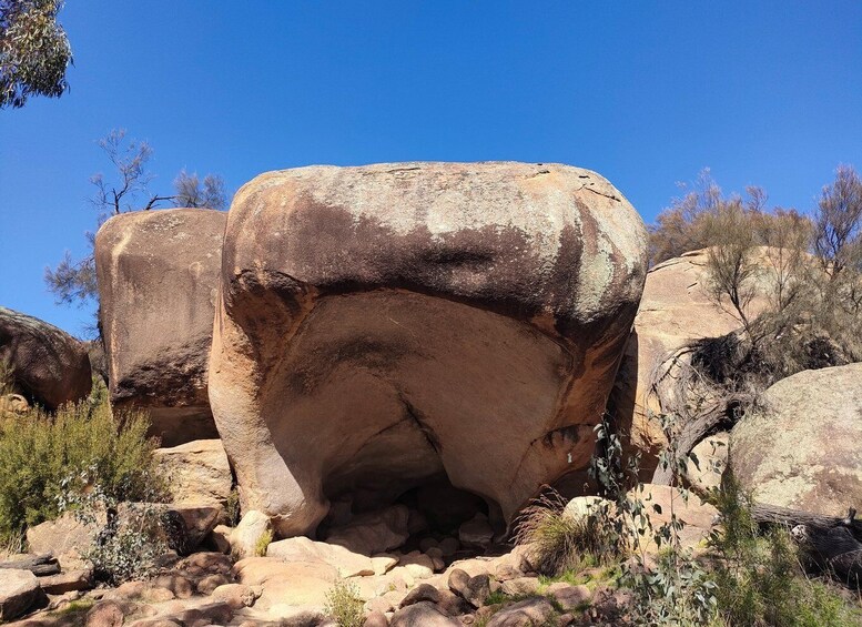 A large rock formation with a cave-like opening surrounded by smaller rocks and sparse vegetation. 4